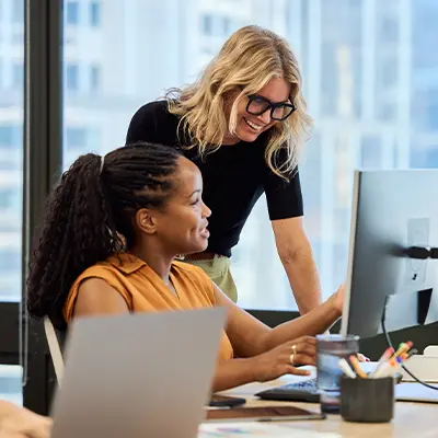 Two women talking in front of a computer screen