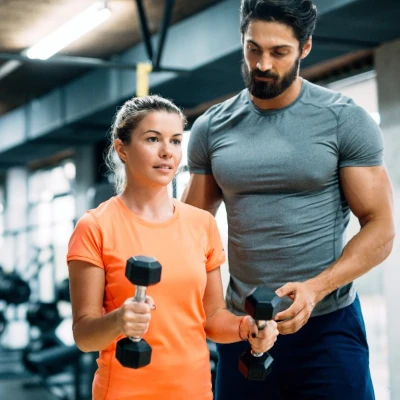 Male fitness trainer working with woman holding dumbbells